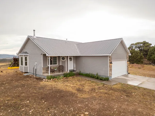 Light gray siding exterior with a gray metal roof, stone accents, an attached garage, a covered front porch, and a bay window