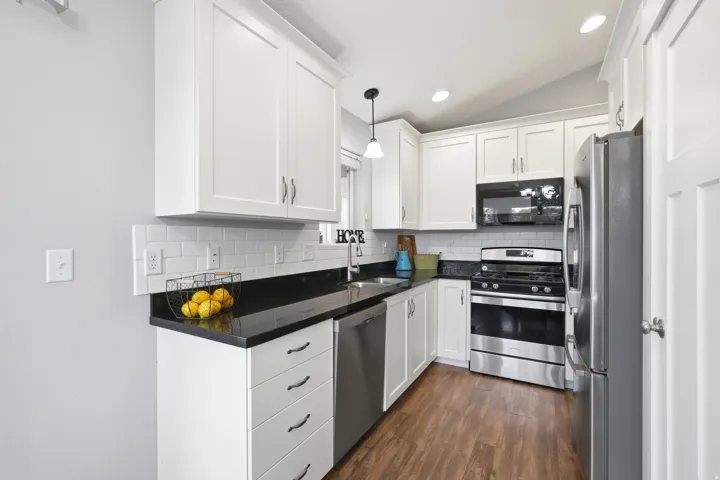 Kitchen featuring white shaker-style cabinetry, granite countertops, a subway tile backsplash, stainless steel appliances including a gas stove, and LVP flooring