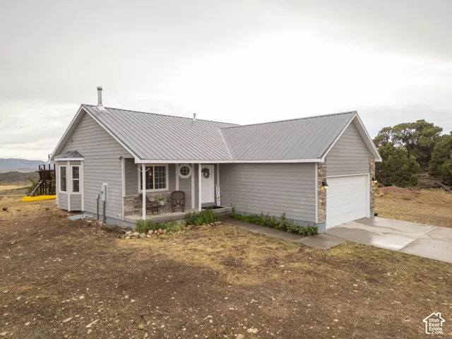 Light gray siding exterior with a gray metal roof, stone accents, an attached garage, a covered front porch, and a bay window