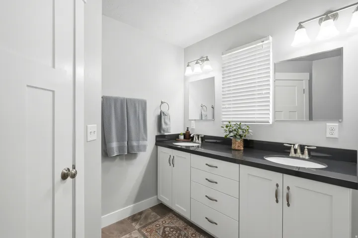 Spa-inspired primary bathroom showcasing a dual-sink vanity with white cabinetry, black granite countertops, and polished chrome fixtures