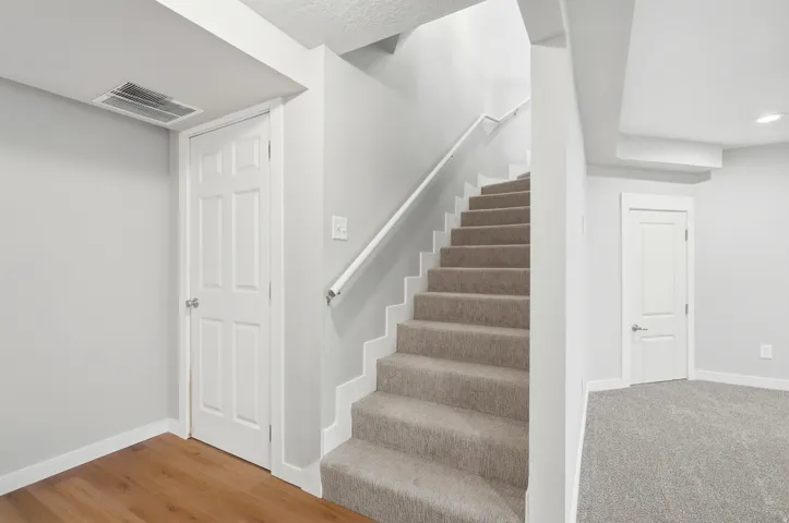 Carpeted staircase with white handrail, wood-finish flooring, and access to utility room