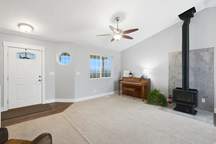 Vaulted ceiling with a ceiling fan, wood-burning stove with tile surround, octagonal window, and a multi-pane window