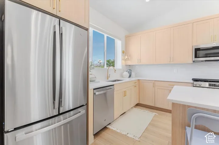 Stainless steel appliances, light wood-finish cabinetry, white countertops, subway tile backsplash, and light wood-finish flooring