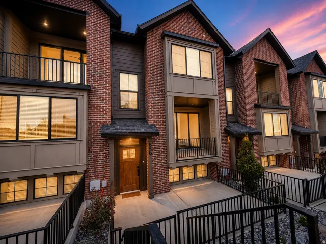 Brick veneer exterior with dark siding accents, multiple balconies with black railings, wood-paneled entry door, and a covered entry
