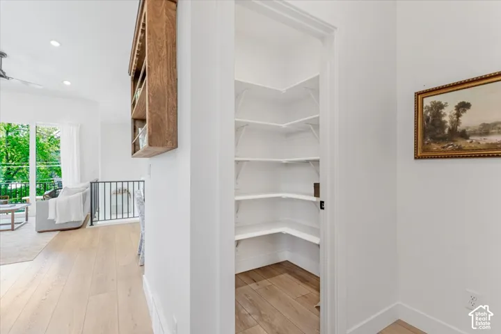 Walk-in pantry with white shelving, wood-finish flooring, and white walls