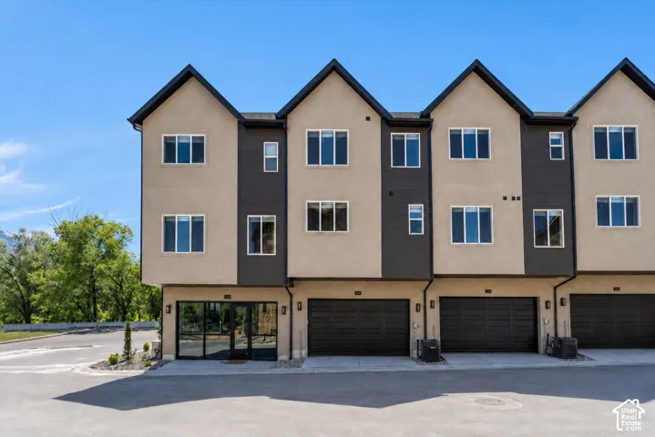Modern townhome exterior with mixed material facade, large windows, and a black paneled garage door