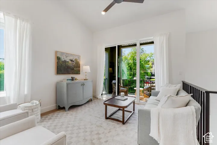 Vaulted ceiling with a ceiling fan, sliding glass doors to a balcony, and light wood-finish flooring