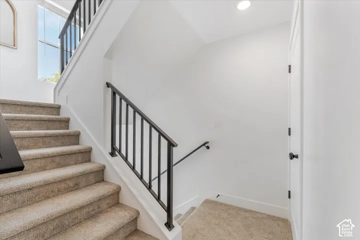 Carpeted staircase with black metal railings, white walls, and recessed lighting