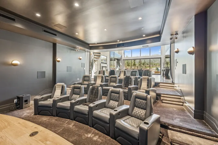 Tiered home theater featuring built-in wall sconces, integrated ceiling lighting, recessed speakers, and dark tone carpeting