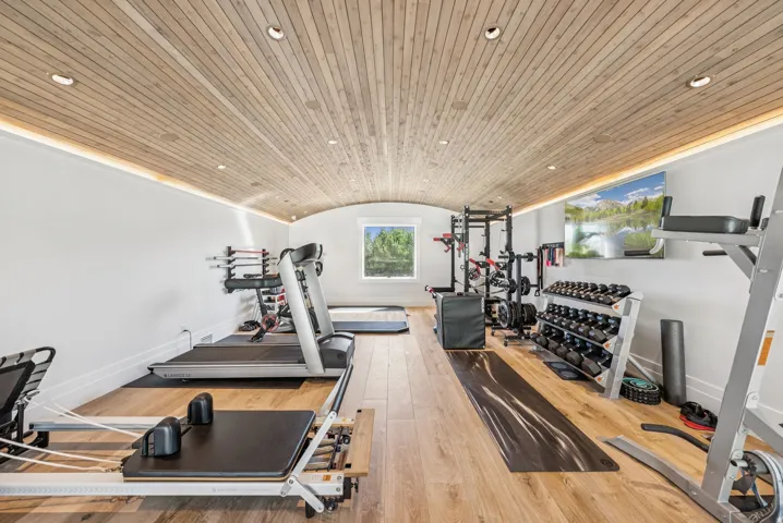 Dedicated fitness area featuring wood-finish flooring and a barrel-vaulted ceiling with integrated recessed lighting