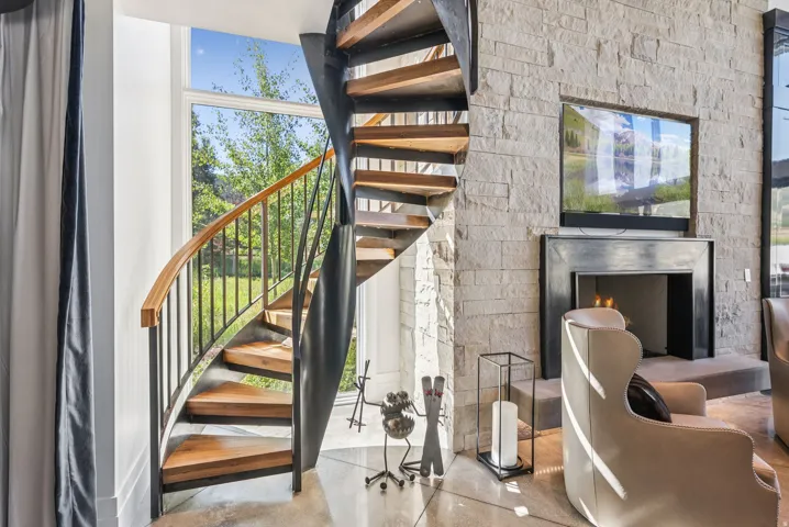 Modern interior showcasing a striking spiral staircase with wood treads and black metal framework, anchored by an exposed brick accent wall