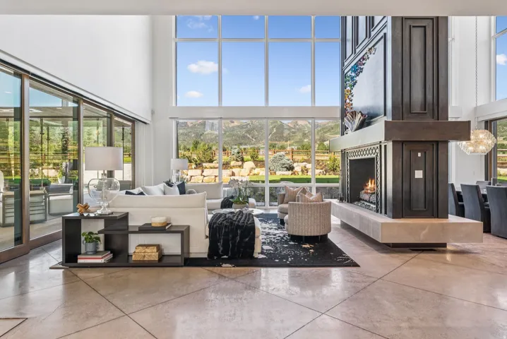 Living space featuring a full-height stone fireplace with a dark wood-finish surround, extensive floor-to-ceiling windows, and polished concrete flooring