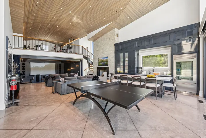 Open-concept living area featuring a wood-panel vaulted ceiling, a large kitchen island with seating, dark cabinetry with glass accents, and a built-in stainless steel refrigerator