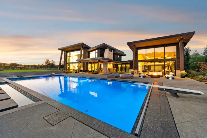 Modern exterior featuring expansive glass walls, a large swimming pool with a diving board, and a fire pit area