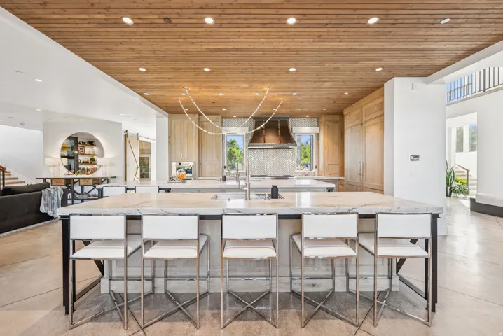 Gourmet kitchen featuring a wood-panel ceiling, double island with stone countertops, integrated appliances, and a chevron-patterned tile backsplash