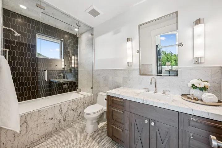 Contemporary bathroom featuring a dark hexagonal tile shower surround, glass shower enclosure, and a built-in tub with marble-look paneling