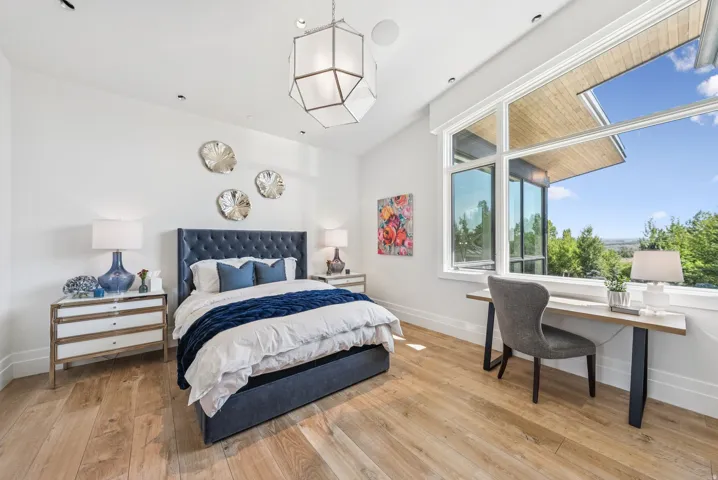 Bright primary bedroom showcasing a navy tufted upholstered bed frame, wood-finish flooring, and abundant natural light from expansive multi-pane windows
