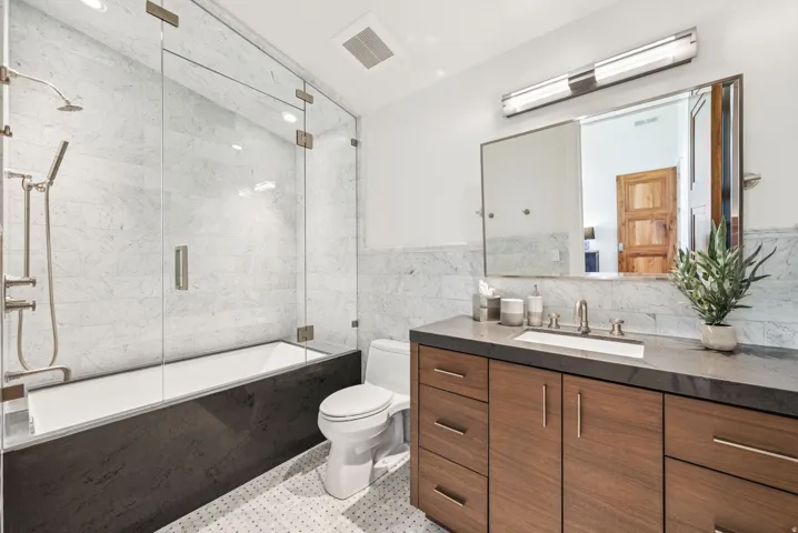 Contemporary bathroom featuring a wood-finish vanity with an integrated basin, a dark countertop, and a full-width mirror