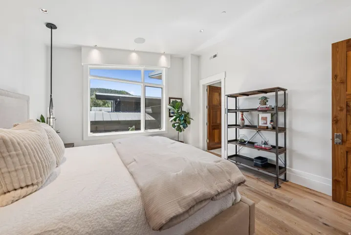 Bright bedroom showcasing hardwood flooring, abundant natural light from expansive windows, and a pendant light fixture