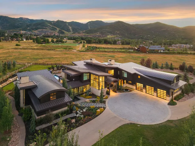 Modern architectural residence showcasing a striking curved driveway, dark exterior cladding with metal roofing, and expansive glazing with integrated yellow-toned lighting throughout