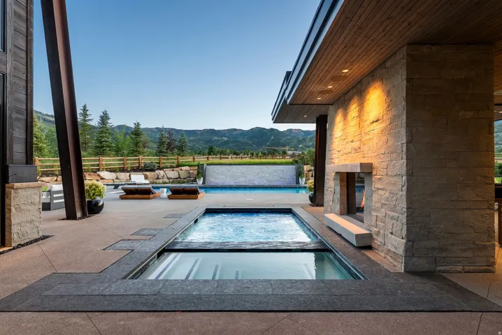 Outdoor living space featuring a built-in spa, rectangular swimming pool with a stone waterfall, outdoor fireplace with a hearth, and a wood-paneled ceiling with recessed lighting