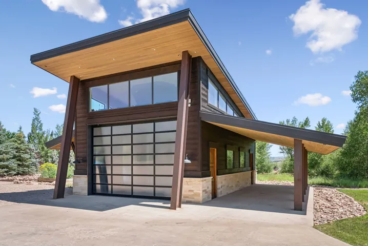 Modern exterior featuring a full-view garage door, wood-paneled soffits, expansive windows, wood-look siding, and a covered portico