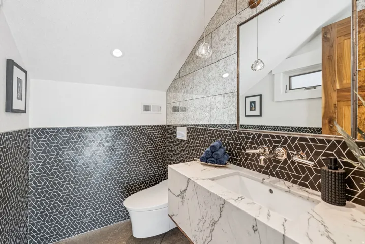 Spa-inspired primary bathroom showcasing a geometric patterned tile accent wall, dual marble-finish vanity with integrated sinks, contemporary chrome fixtures, and a separate water closet