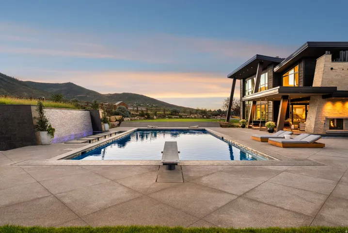 Expansive concrete patio with a rectangular swimming pool featuring a diving board