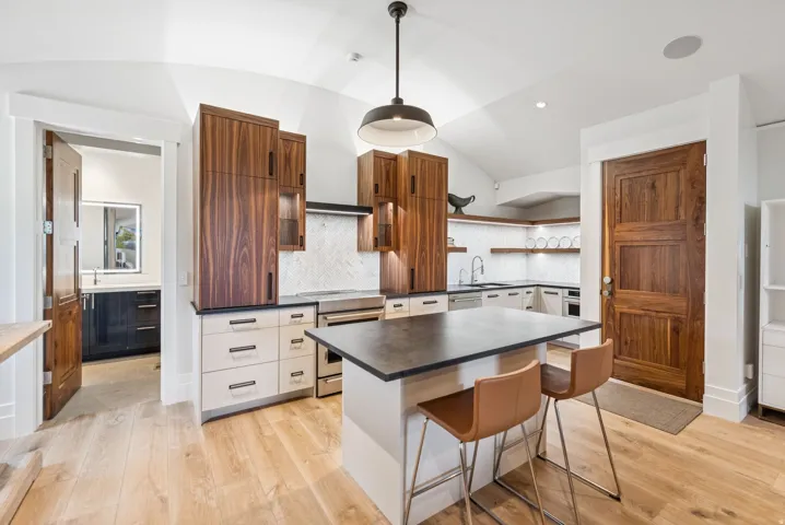 Contemporary kitchen featuring light wood-finish flooring, a vaulted ceiling, and a central island with a dark countertop