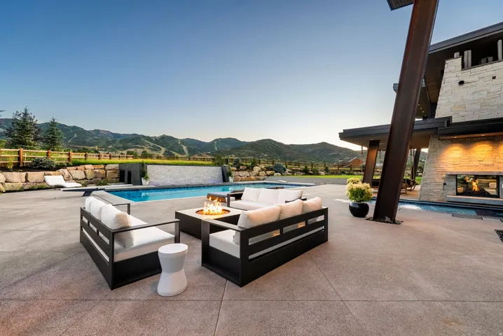 Expansive outdoor living space featuring a resort-style saltwater pool, integrated fire pit with seating area, and custom black metal lounge furniture with cushioned seating