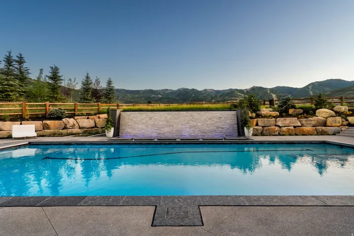 Resort-style saltwater pool featuring crystal-blue waters, surrounded by natural stone decking and anchored by a raised spa with integrated waterfall feature