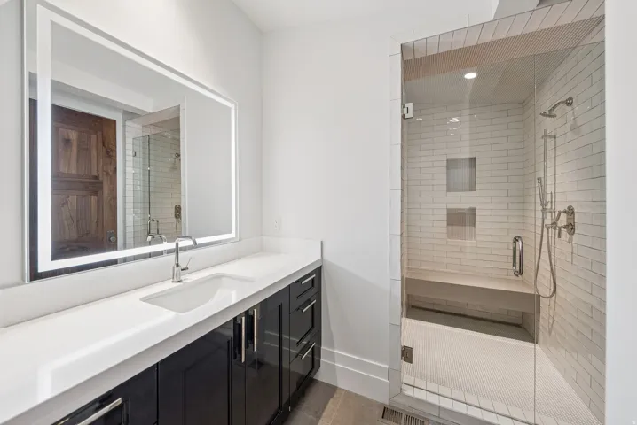 Spa-inspired primary bathroom featuring a floating vanity with white quartz countertop, matte black hardware, and an illuminated mirror