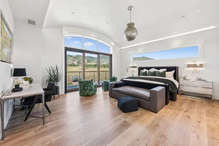Expansive room featuring light wood-finish flooring, a wall of glass doors opening to a balcony, and a large horizontal window