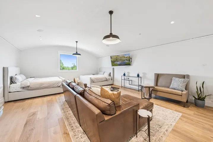Bright, open loft-style living space featuring soaring vaulted ceilings with pendant lighting, hardwood flooring throughout, and multiple seating areas