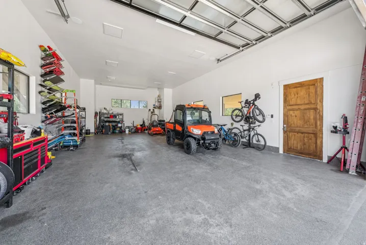 Spacious garage featuring a high ceiling, exposed garage door track system, multiple windows for natural light, a wood-finish interior door, and concrete flooring