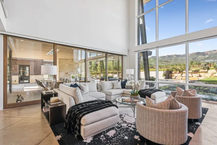 Living area featuring expansive floor-to-ceiling windows, high ceilings, polished concrete flooring, and sliding glass doors opening to outdoor spaces