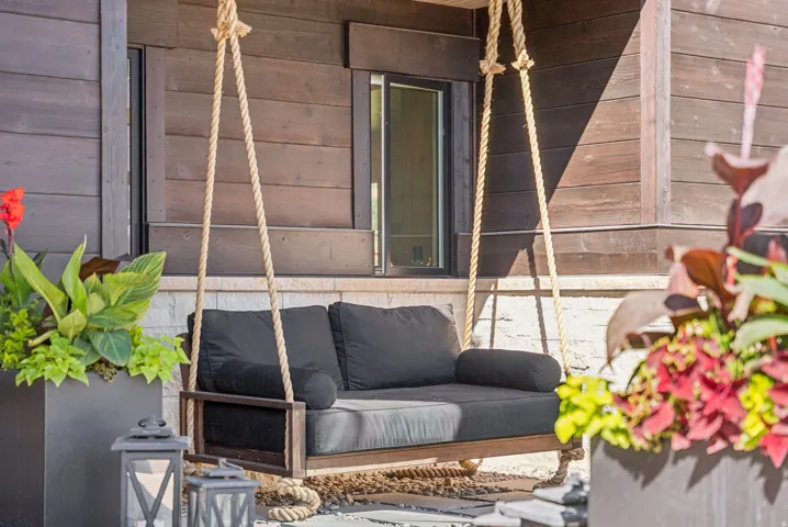 Covered outdoor living space featuring a suspended rope-swing daybed with deep cushioning, natural jute rigging, and weather-resistant upholstery