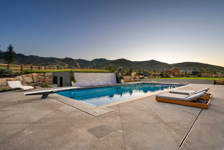 Expansive outdoor living area featuring a rectangular swimming pool with integrated diving board, a stone retaining wall, and a water feature