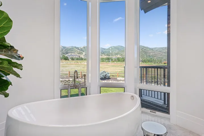 Freestanding soaking tub featuring a floor-mounted faucet, surrounded by large vertical windows with mountain and landscape scenery