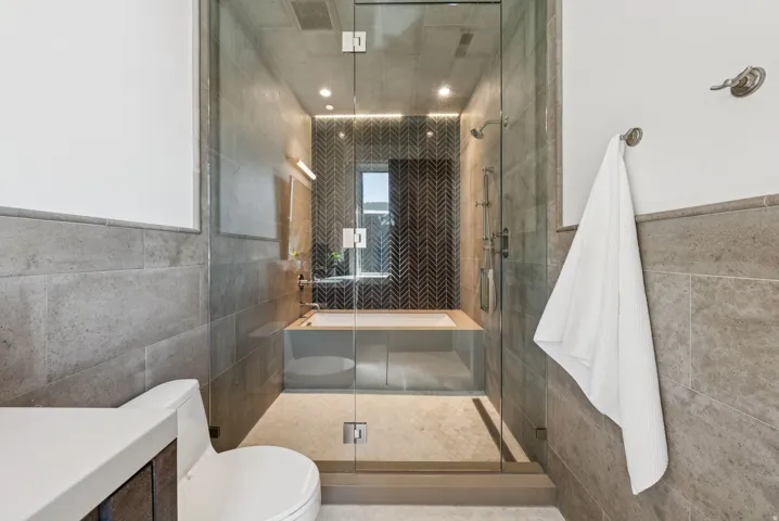 Contemporary bathroom featuring a glass-enclosed shower with a built-in tub, dark herringbone tile accent wall, recessed lighting, and large format wall tiling
