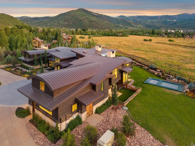 Contemporary architectural design featuring a curved metal roof, extensive landscaping, and a covered outdoor pool