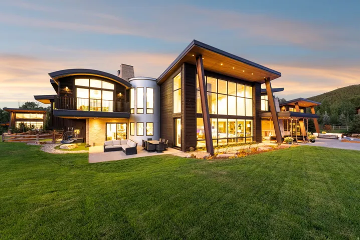 Modern architectural residence featuring expansive floor-to-ceiling windows, curved glass walls, and a striking geometric design with integrated outdoor lighting
