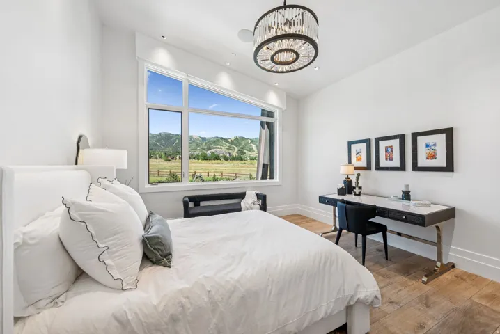 Bright, light-filled bedroom with expansive windows framing pastoral scenery, hardwood flooring, and a decorative pendant ceiling fixture