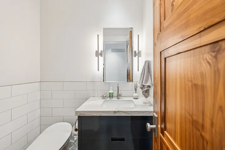 Bathroom featuring white subway tile wainscoting, a dark wood-finish vanity with a white countertop, an undermount sink, and a mirrored medicine cabinet flanked by modern vertical sconces