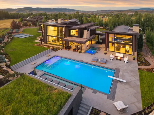Modern architectural residence featuring extensive glass facades, a large geometric swimming pool with integrated lighting, and a separate elevated hot tub