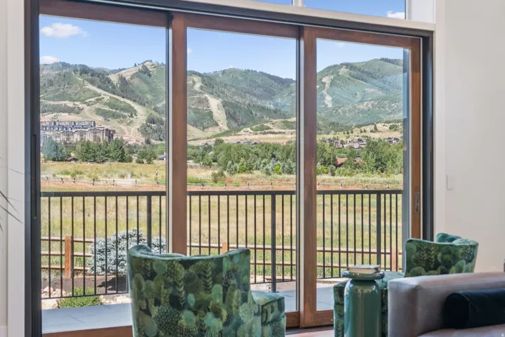 Large format sliding glass doors with dark wood frames open onto a balcony with black metal railings, offering expansive mountain scenery