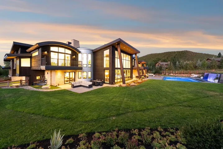 Modern architectural residence showcasing curved glass walls, multiple gabled rooflines, and expansive glazing that floods interior spaces with natural light