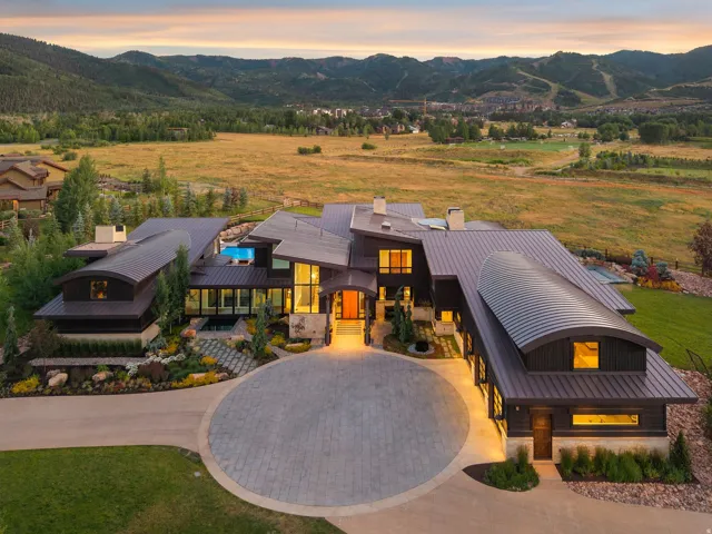 Contemporary architectural residence featuring a metal roof, expansive windows, a circular paver driveway, and an outdoor pool