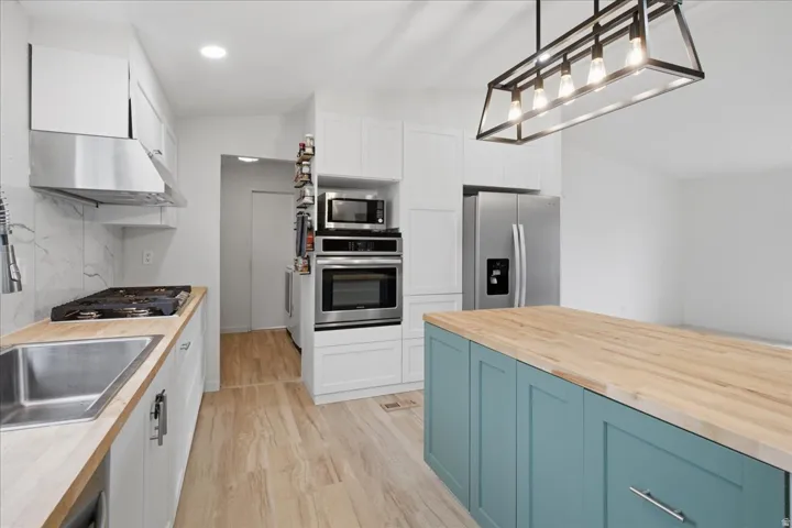 Kitchen featuring a gas range, stainless steel appliances, wood-finish flooring, white cabinetry, and a central island with a wood countertop