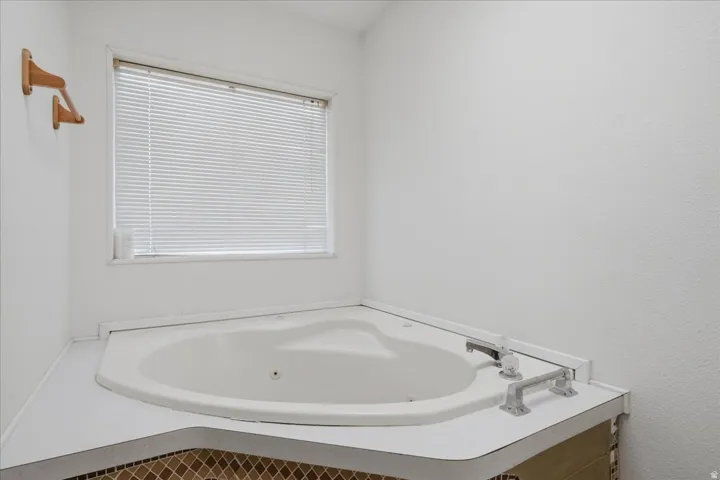 Corner soaking tub with integrated deck, white window blinds, and mosaic tile detailing